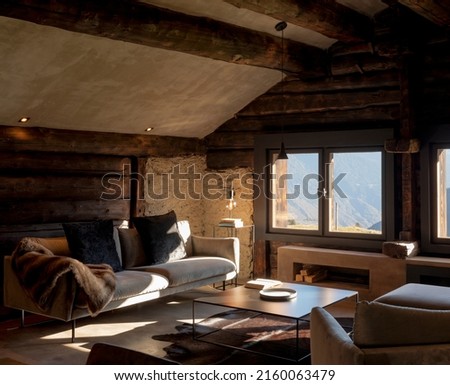 Mountain chalet living room with large sofa, two armchairs and a large window overlooking the Alps. Wooden beams and nobody inside. Royalty-Free Stock Photo #2160063479
