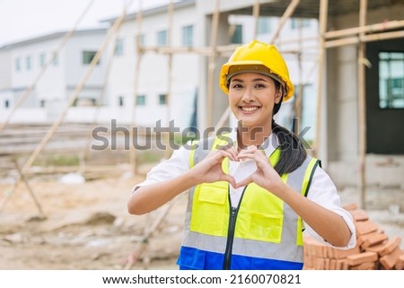 beauty woman hand love sign dressing as engineer worker builder in construction site background