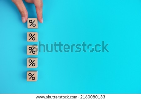 Hand arranging wood block stacking with icon percentage symbol upward direction, on a blue background.               
