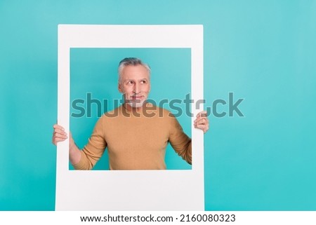 Portrait of minded senior man hold paper window look interested empty space isolated on turquoise color background