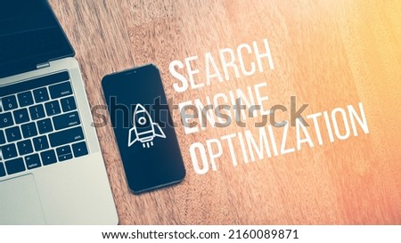 Concept Search Engine Optimization or SEO. Text with rocket icon on smartphone next to laptop
