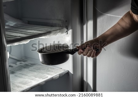 Hand introducing a saucepan with hot water to thaw the ice in the fridge. Royalty-Free Stock Photo #2160089881