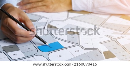 Man holding a pencil pointing to cadastral map to decide to buy land. real estate concept with vacant land for building construction and housing subdivision for sale, rent, buy, investment Royalty-Free Stock Photo #2160090415