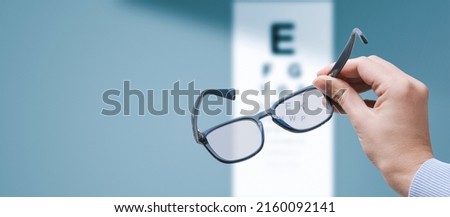 Professional optometrist holding glasses and eye chart in the background, eyesight and vision problems concept, copy space Royalty-Free Stock Photo #2160092141