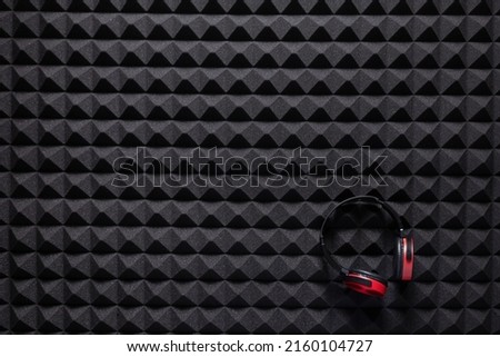 Music headphones at acoustic foam panel background texture. Music equipment concept in studio