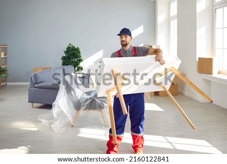 Strong young man from a moving company or truck delivery service carrying a white wooden table while removing furniture from a modern house or apartment Royalty-Free Stock Photo #2160122841