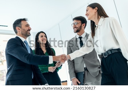 Shot of business people shaking their hands while smiling after signing new contract in modern startup office.