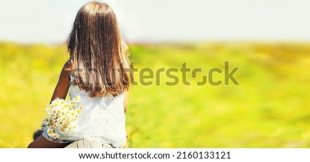 Rear view, silhouette little girl child sitting with flowers enjoying nature on summer blurred background in the park, blank copy space for advertising text