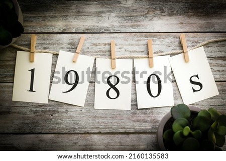 A set of printed cards spelling the word 1980s on an aged wooden background.