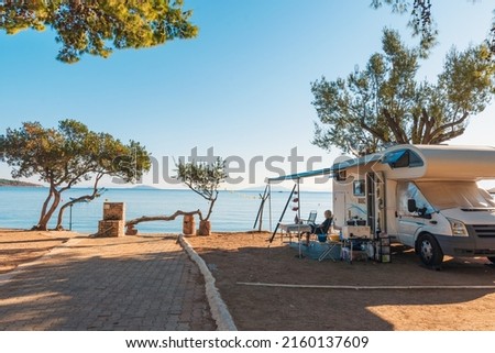 Family traveling with motorhome are eating breakfast on a beach. Travelers on an active family vacation with motorhome RV parked on the beach under a tree facing the sea, Crete, Greece. Royalty-Free Stock Photo #2160137609