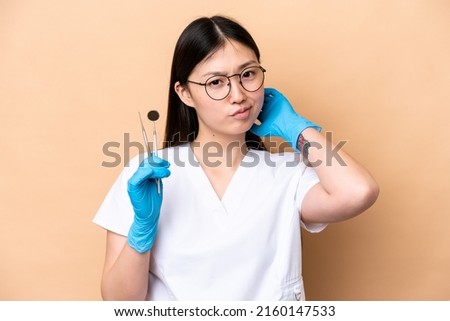 Dentist Chinese woman holding tools isolated on beige background having doubts