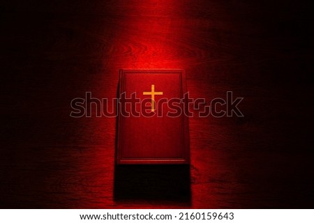 The Bible in a beam of red light. Religion and faith. Christian literature. A bible on a wooden table. Protestantism, Catholicism, and Orthodoxy. Reading religious literature.