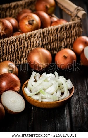 Pieces of onion in a plate and whole onions in a box. On a wooden background. High quality photo
