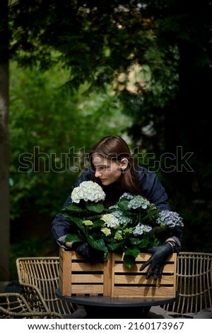 portrait of a young beautiful florist hugging a bouquet of beautiful flowers in a wooden pot on the table in the garden