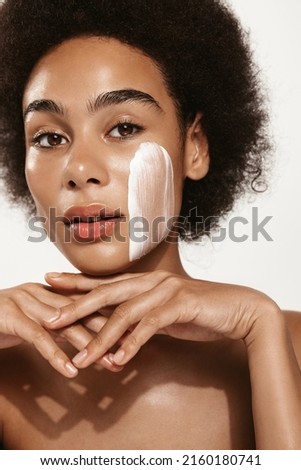 Skin care. Close up of young african american woman touching her face to apply moisturizer. Face of Black girl with daily cream, facial cosmetics, pink background.