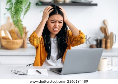 Frustrated sad puzzled Asian brunette girl, freelancer or designer, got a negative result, failed the project, looks desperately at laptop screen, holds her hands on her head, have stressed situation Royalty-Free Stock Photo #2160194489