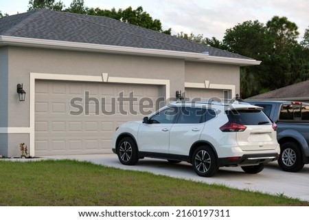 Car parked in front of wide garage double door on concrete driveway of new modern american house Royalty-Free Stock Photo #2160197311