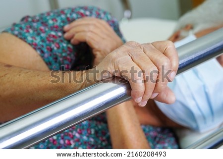 Asian elder senior woman patient holding bed rail while lie down with hope waiting her family in hospital. Royalty-Free Stock Photo #2160208493