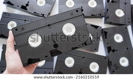 Hands holding a VHS tape back side with scattered tapes in the background.