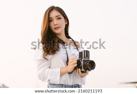 Beautiful Asian girl blogger influencer holding analog vintage film camera relaxed with happy on the rooftop at sunset time of a building, Creates content for social media channels and applications.