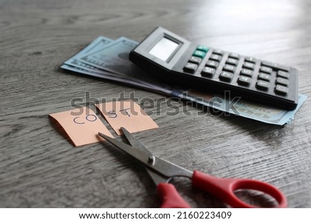 Selective focus image of scissor, calculator, money and note with text COST. Financial, cost cutting, reduce expenses concept