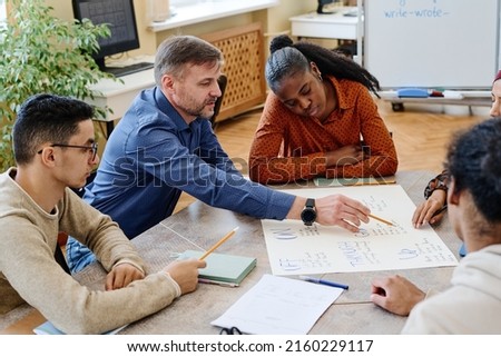 High angle of modern teacher and his immigrant students working on educational English language poster together in group Royalty-Free Stock Photo #2160229117