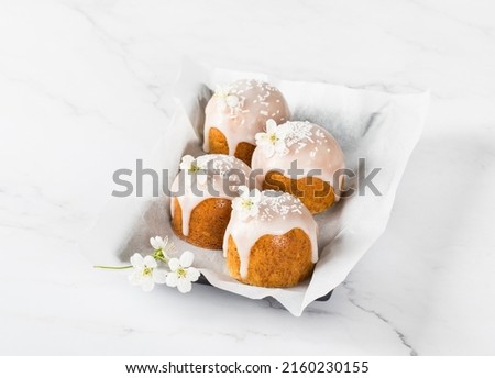 Little Cakes with white sugar glaze, decorated with a flower and confectionery sprinkles, on a serving plate. Light background