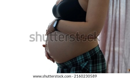 Closeup of Pregnant Woman Touching her Belly over the Window. Motherhood, Preparation and Expectation of Baby Concept