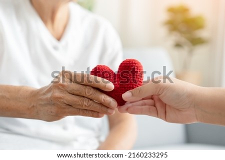 Young and senior woman holding each other hands and red yarn heart shape togetherness concept. Elderly care and protection with love from grandchild.  Royalty-Free Stock Photo #2160233295