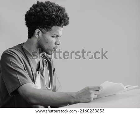 Medical student concentrate on reading text book. Young African American doctor reads documents preparing for exams. Professional health care and medicine occupation. Black and white image photography