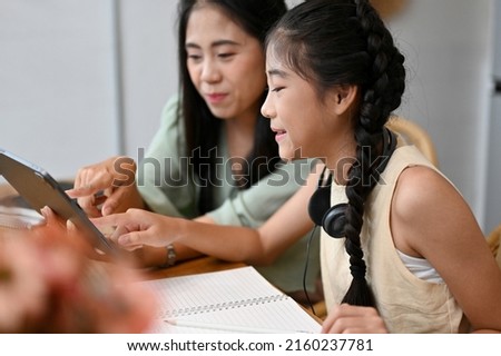 Kind Asian mom watching kids cartoon with her lovely daughter via digital tablet touchpad, at home. close-up image