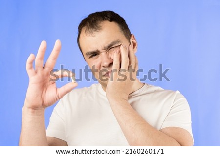 Man in a white T-shirt on a blue background holds a wisdom tooth in his hands after surgical tooth extraction.Man after an operation to remove wisdom teeth.Pain in wisdom teeth, concept of dentistry Royalty-Free Stock Photo #2160260171