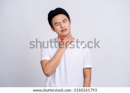 Portrait of young asian man in casual white t-shirt isolated on white background. He had a sore throat and touched his throat. Difficult to swallow. Royalty-Free Stock Photo #2160261793