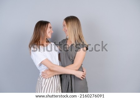 Unity concept. Caucasian daughter hugging her mom, showing her love in casual light clothes. Happy relationship in the family between parents and adult children, studio color wall