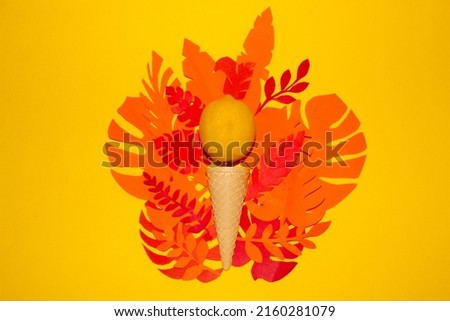 ice cream cone with yellow lemon ball on paper colorful tropical leaves, yellow background, summer design, tropical vocation refreshment