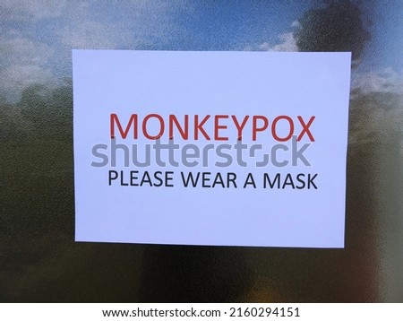 'Monkeypox Please Wear A Mask' wording on A4 paper stuck to reflective speckled glass window. 