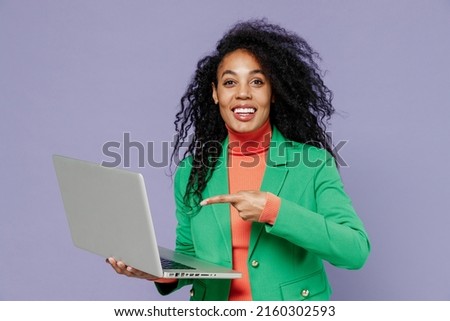 Charming young black curly woman 20s wears green shirt hold use work point index finger on laptop pc computer typing reading searching isolated on plain pastel light violet background studio portrait