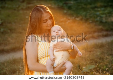 Young mother with newborn baby son on sunset nature background. Motherhood, mother love, parenthood concept