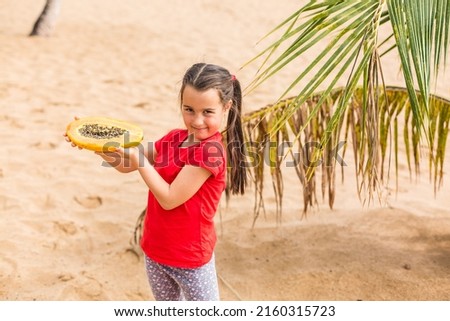 Portrait of a cute little girl with papaya against a background of palm trees