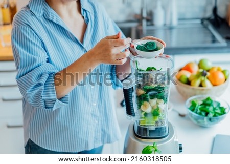 Woman adding spirulina green powder during making green smoothie on the kitchen. Superfood supplement. Healthy detox vegan diet. Healthy dieting eating, weight loss program. Selective focus. Royalty-Free Stock Photo #2160318505