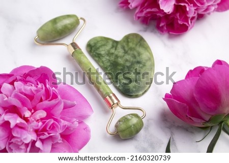 Jade Roller for face massage. Jade Gua sha facial massager tools. Peony flowers. Skin care cosmetic. Beauty concept for face body care