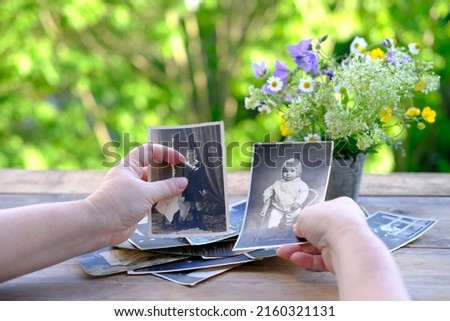 female hands fingering set of vintage photos 1950, photographs on table, bouquet of wild flowers, concept of genealogy, memory of ancestors, family tree, nostalgia, childhood memories, remembering
