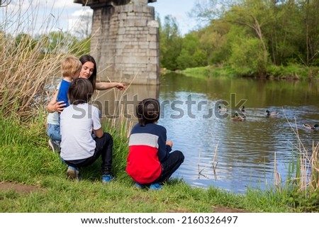 Family with children, feeding ducks in a river in front of old wooden cottage on brick pillar in The Radbuza River, near Chotesov, Czech Republic, Europe