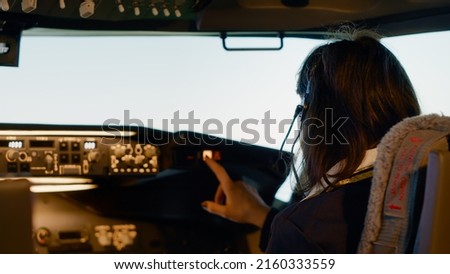 Woman copilot in uniform preparing to takeoff for airline flight, pushing buttons on dashboard and control panel command in cockpit. Flying airplane with aerial navigation and radar. Close up.