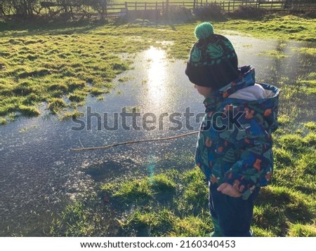 Sunset with boy playing with stick and water wear coat cartoon print and wool hat in the field