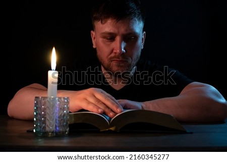 A man reads in the dark with a candle.