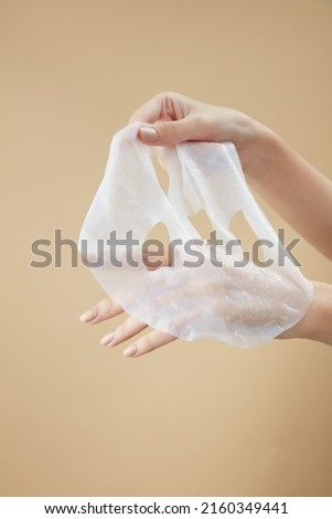 Front view of hand holding a mask in beige background for cosmetic advertising Royalty-Free Stock Photo #2160349441