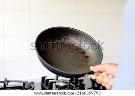 Close up man hand holding dirty  burnt food unclean able stain on the pan in the kitchen.