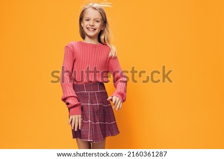 a beautiful, happy girl stands on a yellow background in a pink T-shirt and skirt smiling cutely at the camera. studio photography