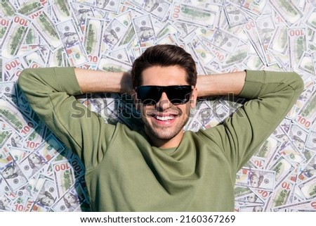 High angle view photo of cheerful man laying usd banknotes hands head isolated on money background